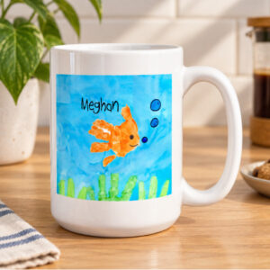 Grande 15 oz ceramic mug with handprint fish artwork sitting on kitchen table