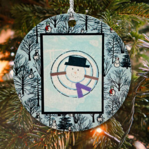 Winter Ornament with snowman artwork hanging in a tree.