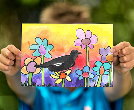 Child holding out artwork of black bird and flowers